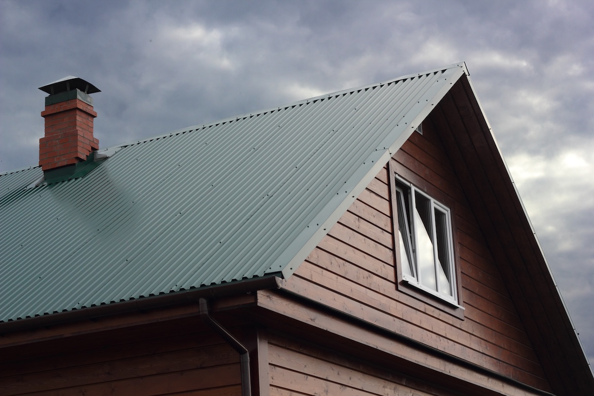 metal roof vs shingles Green metal roof and brick chimney under cloudy sky photo