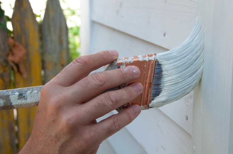 close up view of homeowner painting vinyl siding with a brush