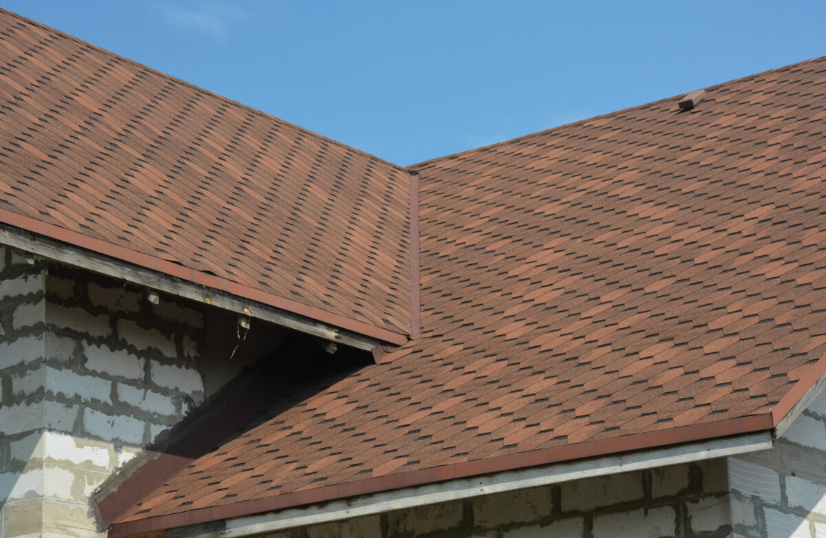 Brown asphalt shingled roof valley leaking problem area with a ventilation cap. A close-up of asphalt shingles installed on a roof valley with a waterproof flashing. Asphalt shingles roofing.
