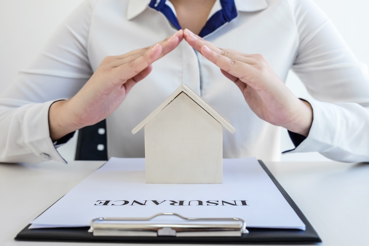 insurance and care protection of house concept, woman with protective gesture of small home model.