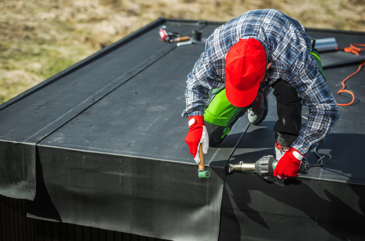 EPDM Membrane Installation on Top of a Garden Shed. Professional Worker Attaching Pieces of Material Using air Blower.