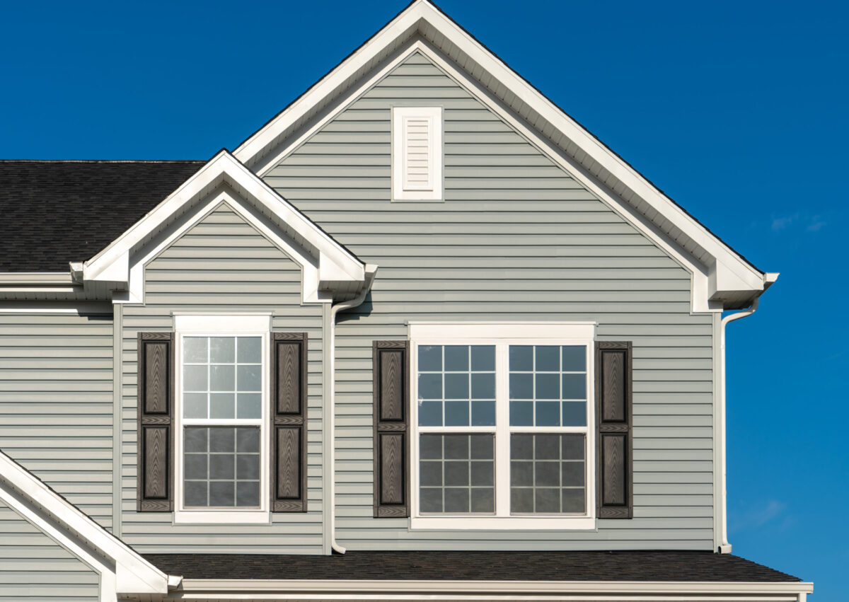 Classic American real estate single family home facade with horizontal vinyl siding, double gable, double and single sash windows, decorative white attic window blue sky background