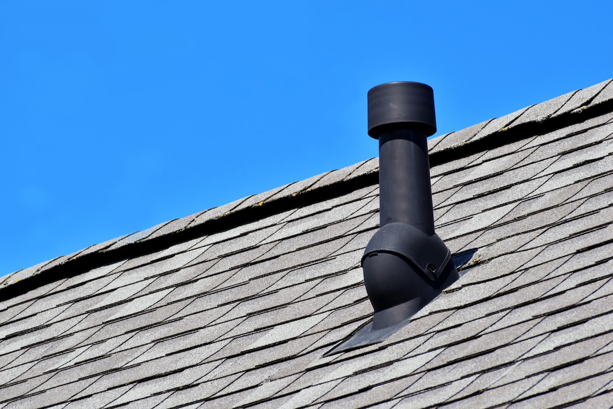 roof vent installation Black air ventilation chimney on grey shingles roof of residental house on blue sky background with copy space for text.