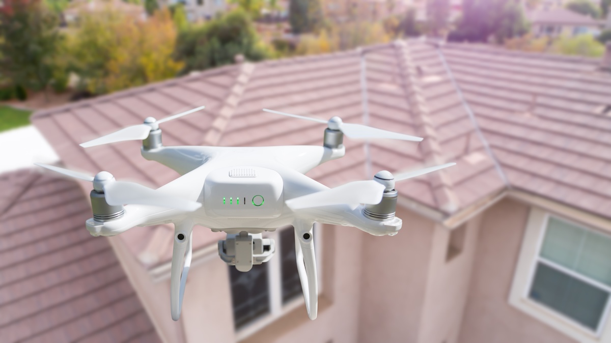 drone roof inspection Unmanned Aircraft System (UAV) Quadcopter Drone In The Air Over House Inspecting the Roof.