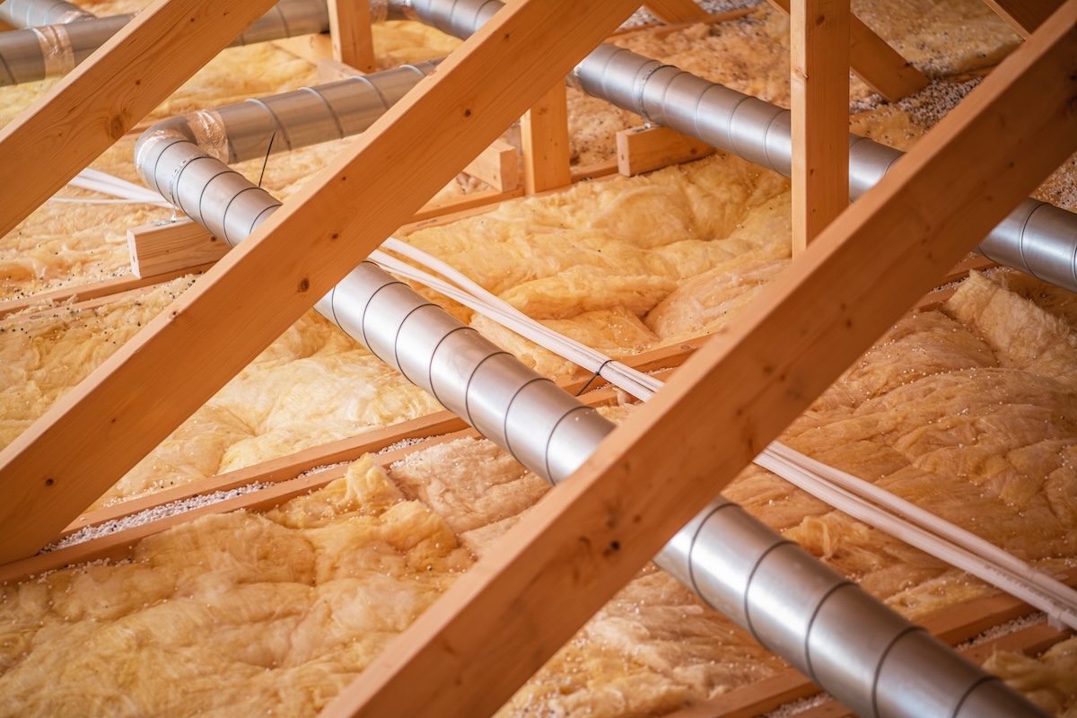 attic insulation Wooden beams support a network of pipes and ductwork, showcasing insulation materials in a residential attic during ongoing construction activities.