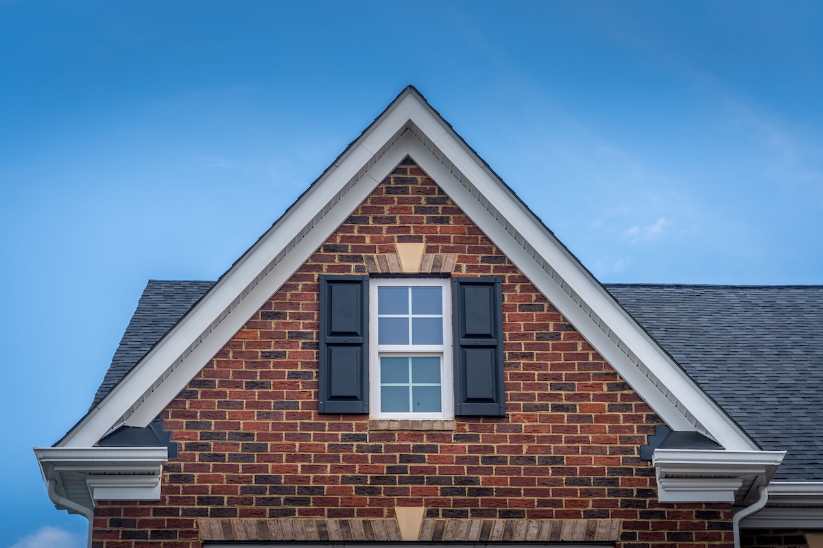 Gable with red brick facade siding, double hung window with white frame, vinyl shutters on a pitched roof attic at a luxury American single family home neighborhood USA