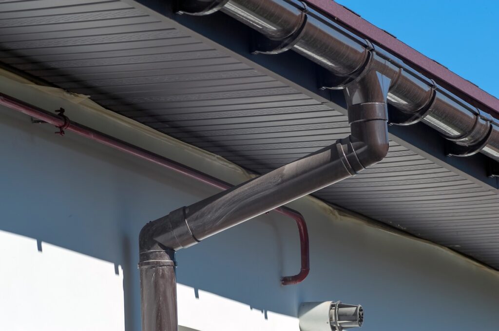 Corner of the house with new gray metal tile roof and rain gutter. Metallic Guttering System, Guttering and Drainage
