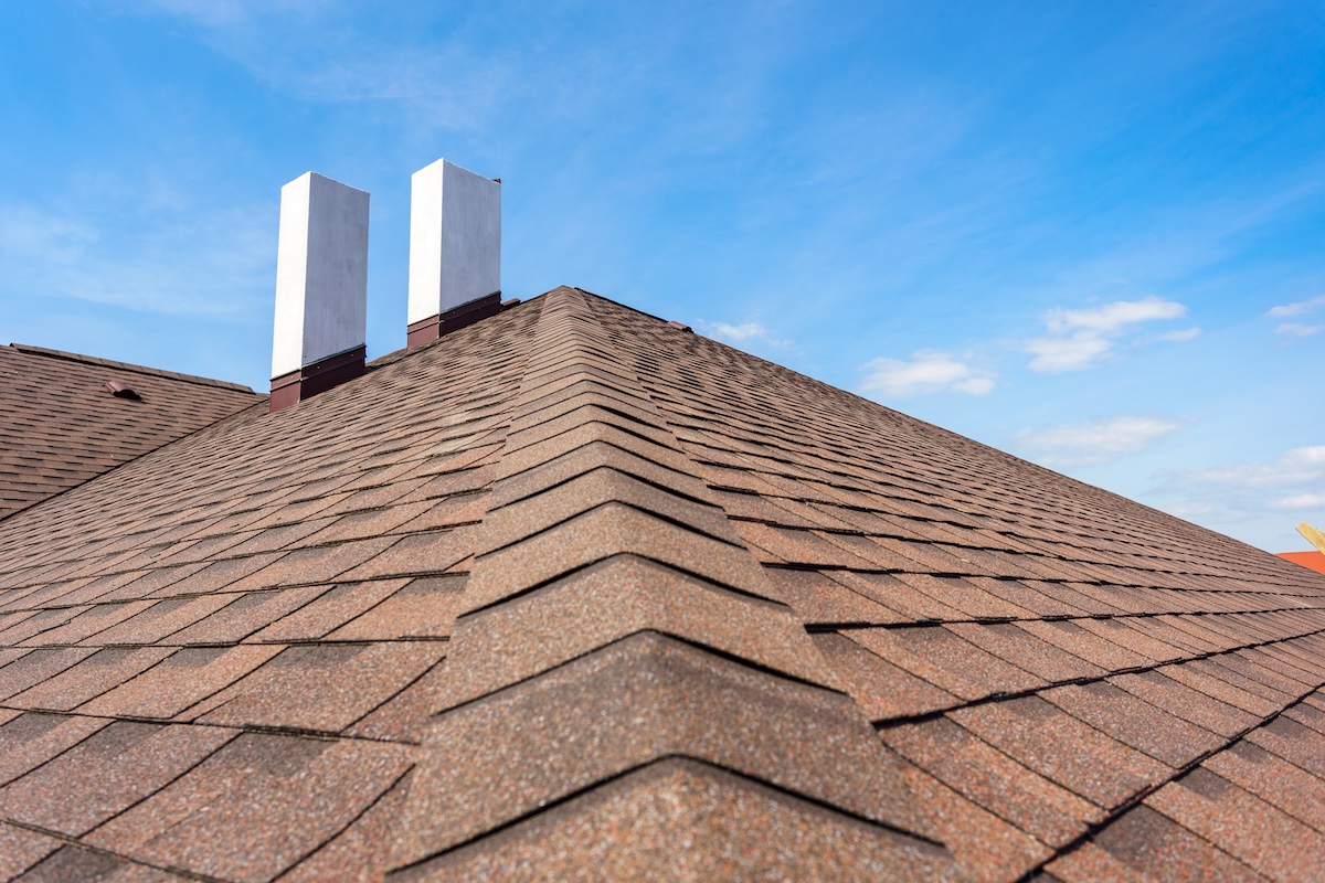 low slope roof Photo of new roof with asphalt tile and two white chimney on new home under construction, against blue sky