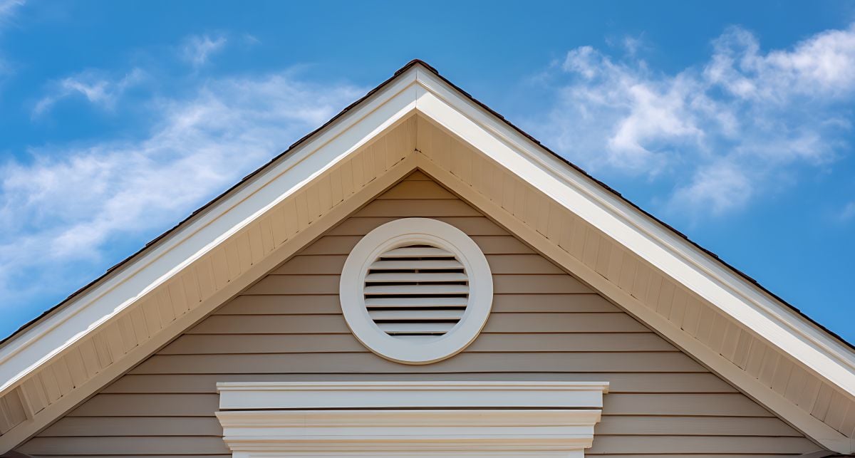 Gable end of a beige house with a round gable vent