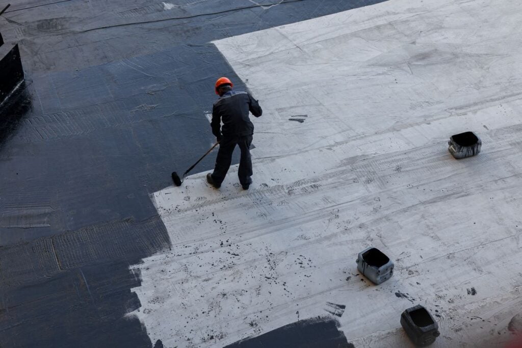 A worker applies bitumen mastic to the foundation