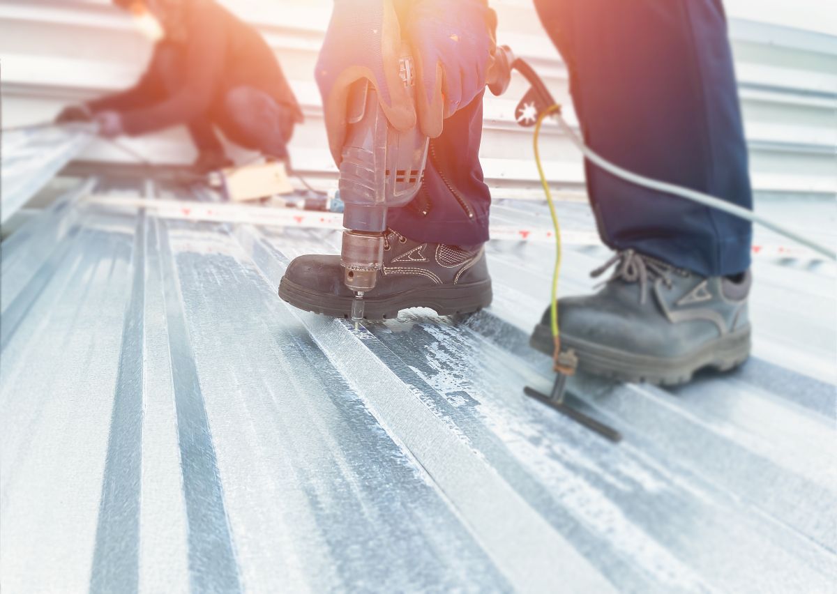 Worker using a nut to screw on the metal roof with a power drill