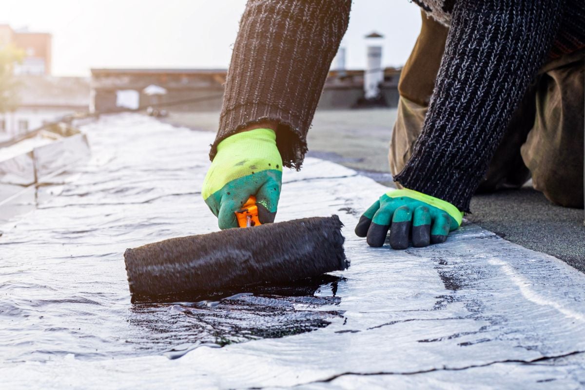 worker treats a roof with bitumen primer before applying rolled asphalt roofing using a torch