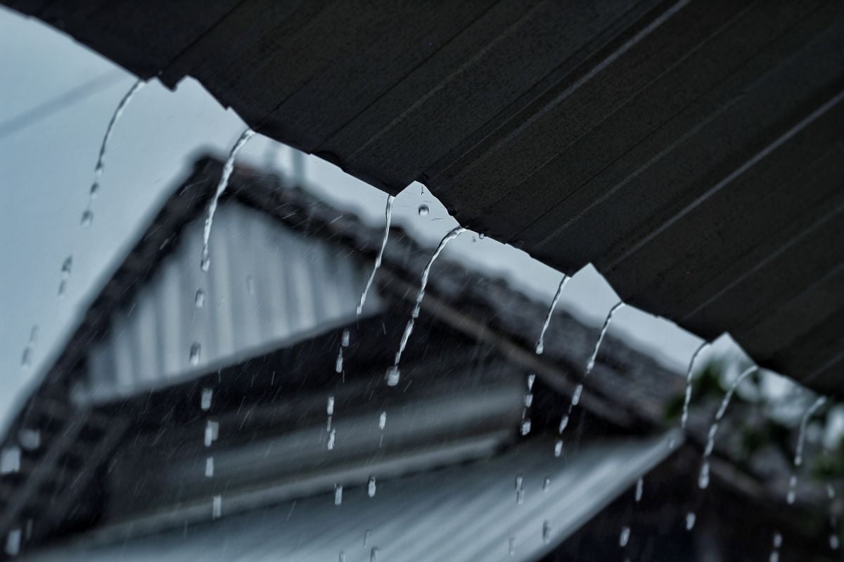 Close-up of heavy rain pouring down from a metal roof against a blurred background