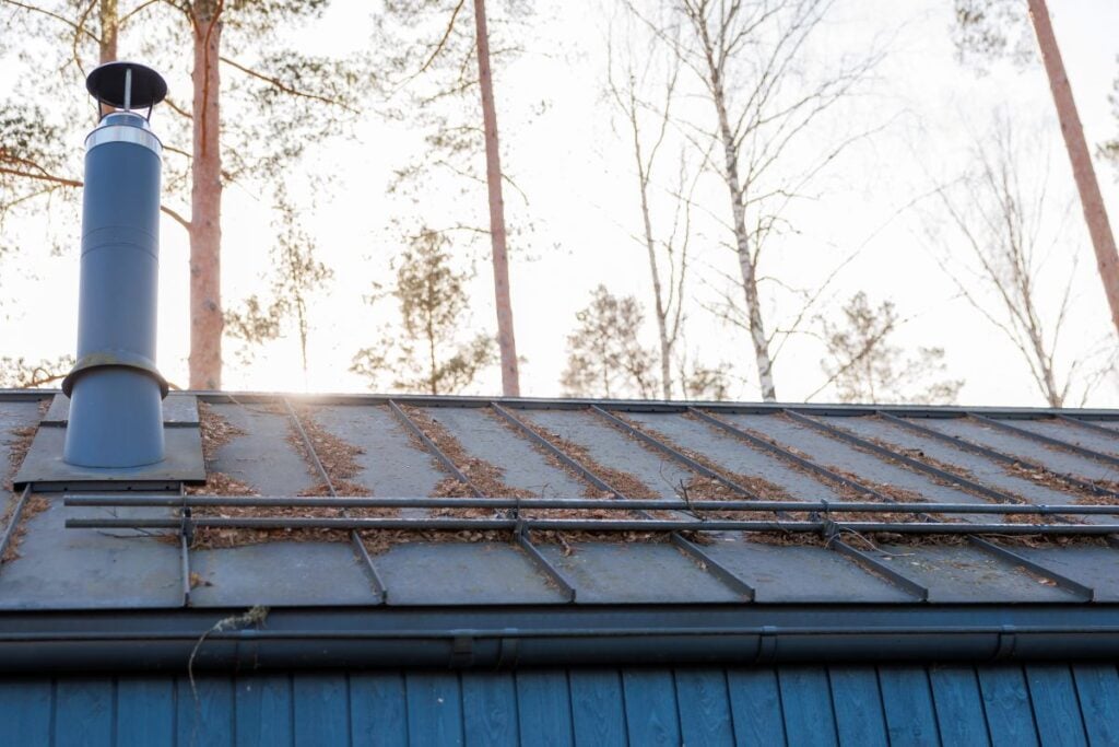 metal roof holds pine needles as a chimney with rain cap rises near the ridge, snow guards span panels